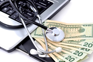 Six $20 bills next to a laptop with a stethoscope on top
