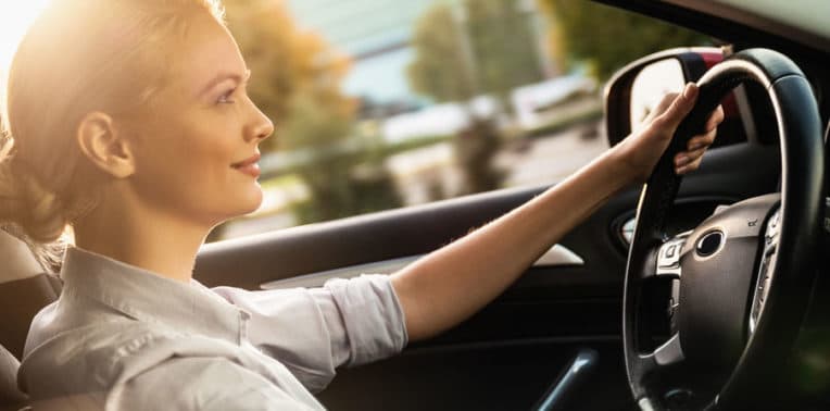 Woman sitting at the wheel of a car with her left hand on the steering wheel