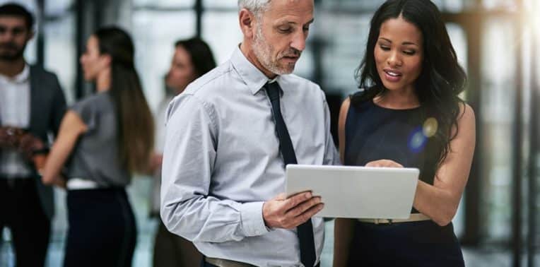 A man and a woman looking at a white tablet with three people in the background