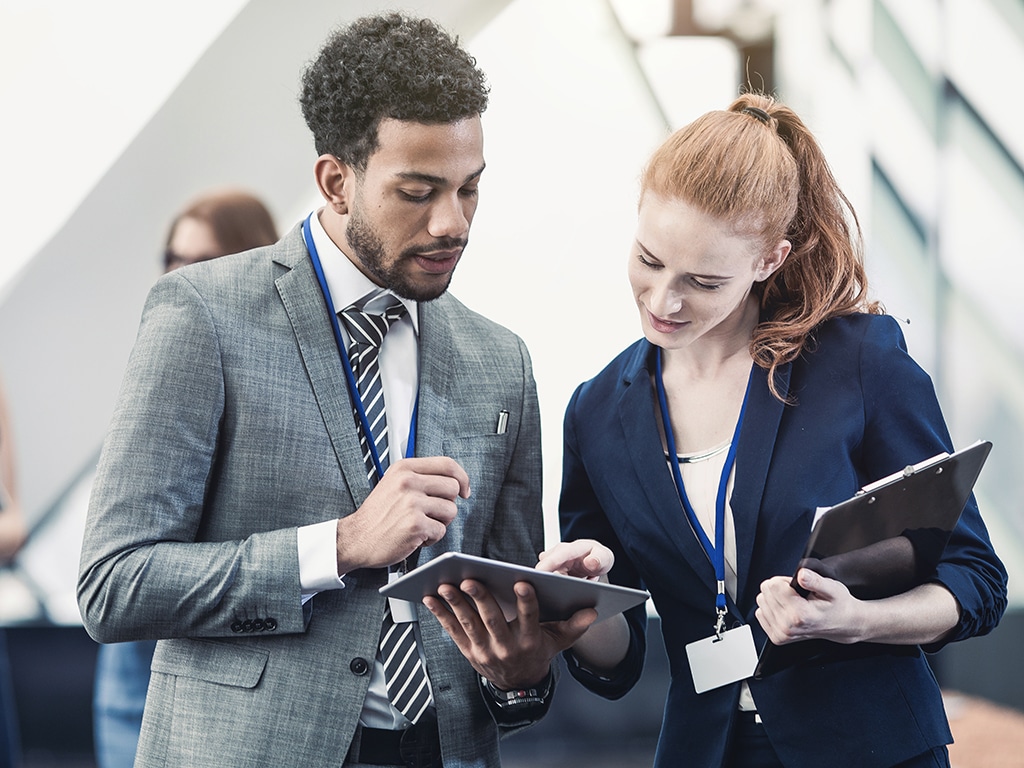 Man holding a tablet for a woman holding a clipboard to look at
