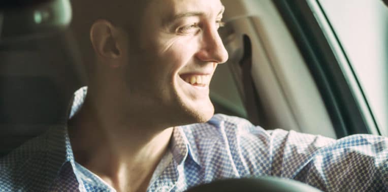 Man at the wheel of a car looking out the window and smiling
