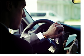 Person with left hand on a steering wheel and right hand holding a cell phone