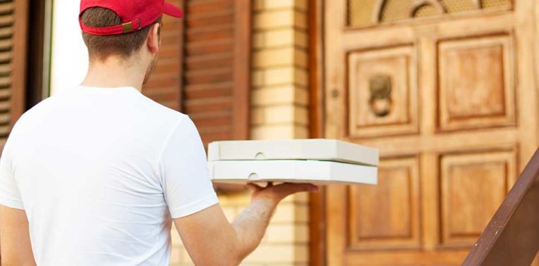Man in a white shirt and red baseball cap delivering two white boxes to a wooden door