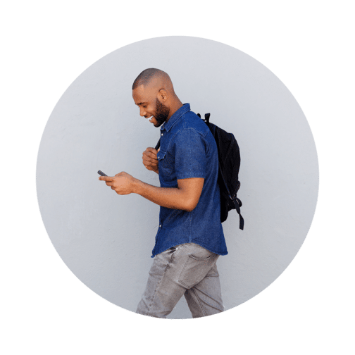 Man walking and carrying a backpack while looking down at a cell phone