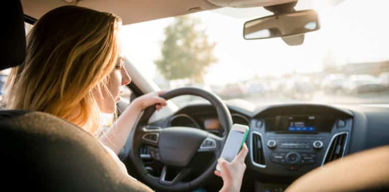 Woman sitting at the wheel of a car looking at a cell phone