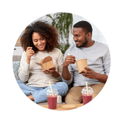 Two people eating from takeout containers with smoothies on the table in front of them