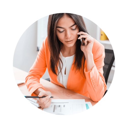 Woman at a desk talking on a cell phone and holding a pen over a stack of paper