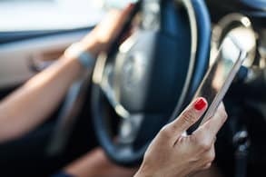 Left hand on a steering wheel and right hand holding a cell phone