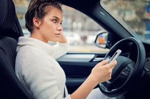 Woman sitting at the wheel of a car holding a cell phone