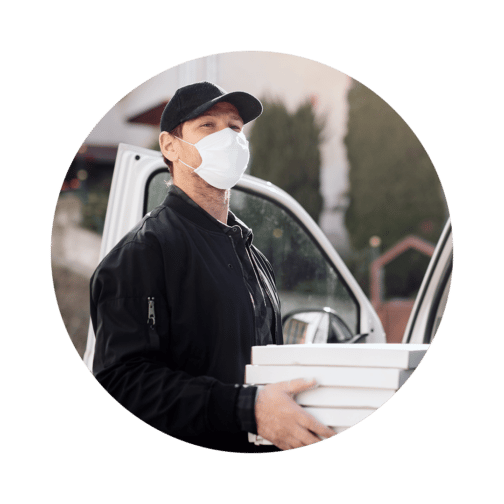 Man wearing a face mask standing in front of an open car door holding a stack of white boxes