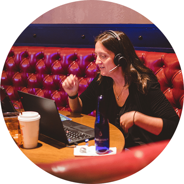 Woman sitting in a red vinyl booth wearing a headset and looking at a laptop screen