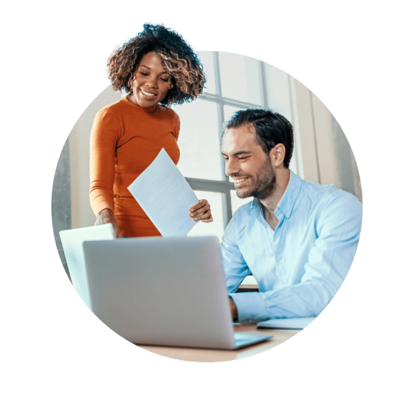 Woman holding papers while pointing at a computer screen where a man is working