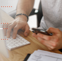 Hands with a cell phone in the left hand and the right hand typing on a keyboard