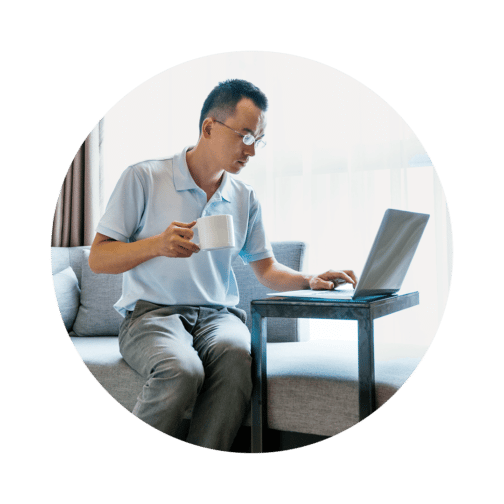 Man sitting on a couch working on a computer with a white mug in his hand