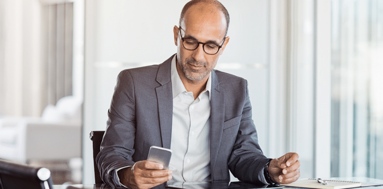 business man at a desk looking at his phone, evoking cell phone reimbursement