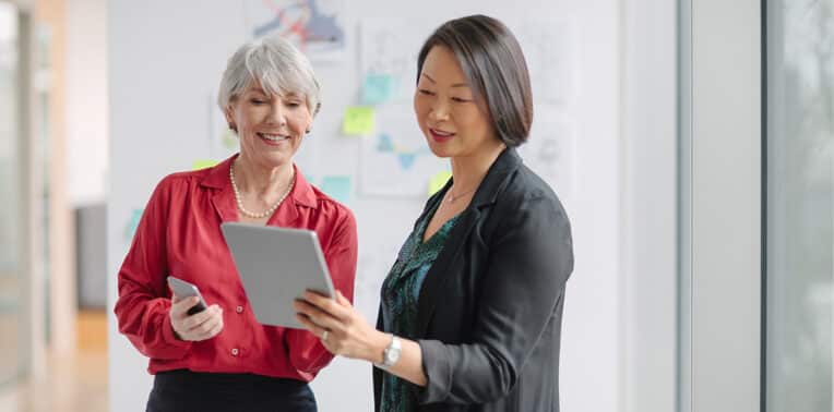 two business women looking at a tablet, evoking BYO Bring your own