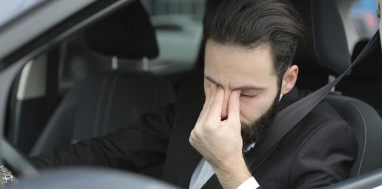 man driving vehicle pinching nose in emotion evoking driver insurance compliance
