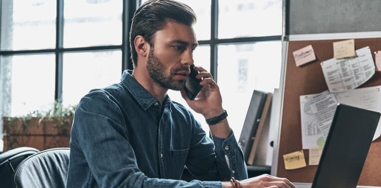 man working from home using phone and laptop evoking implement byo program