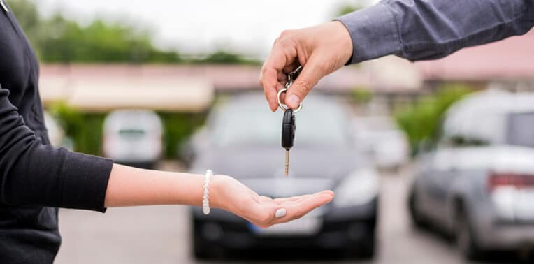 two people in a parking lot, one handing keys to the other, evoking "What to know when selling a car"